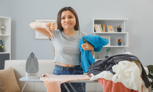 a girl is standing next to a ironing stand and she is not happy to do ironing clothes